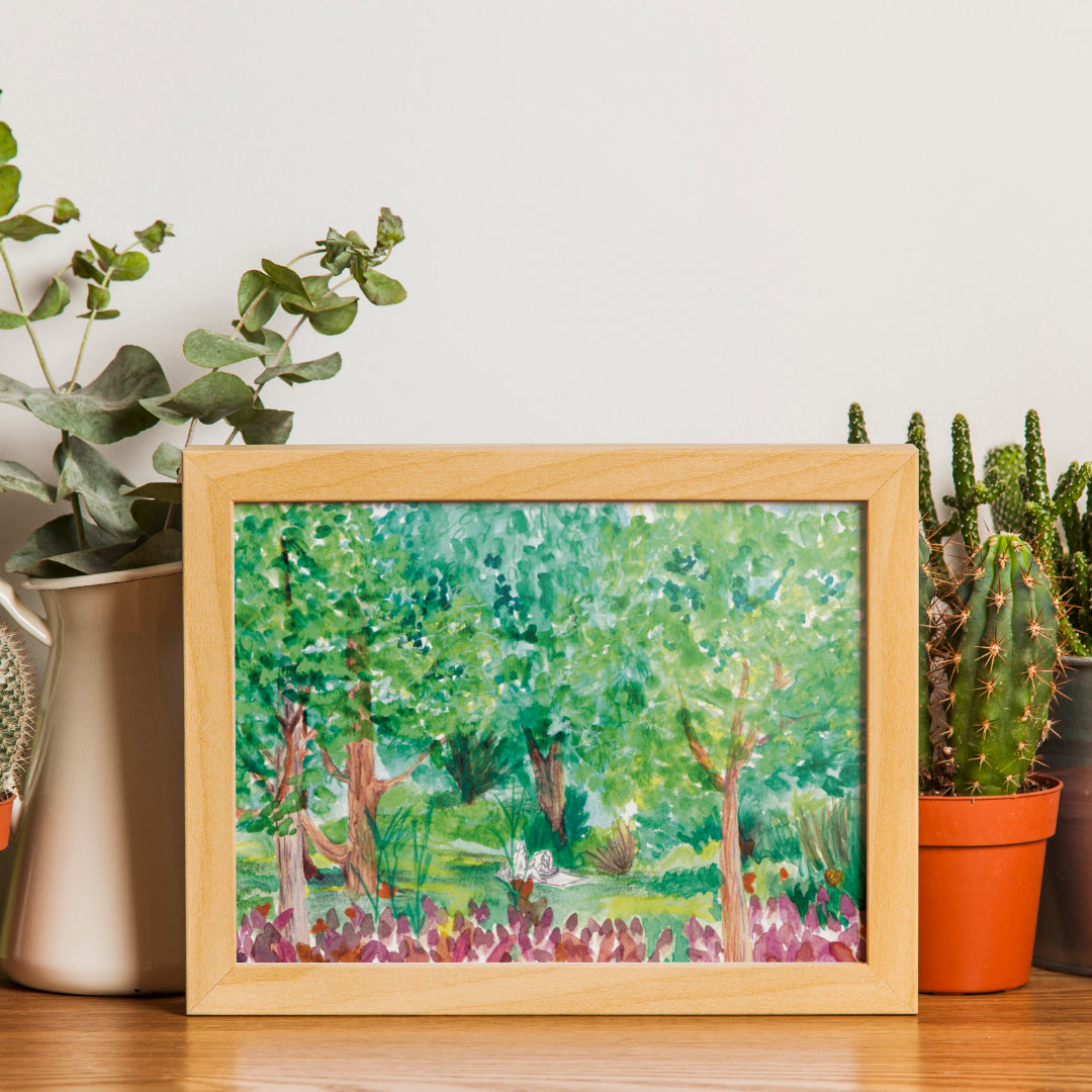 mock up image of the framed giclée print of a watercolour painting made by Verónica Silva, representing a booknic. Two girls seat in the middle of a park, reading and relaxing.